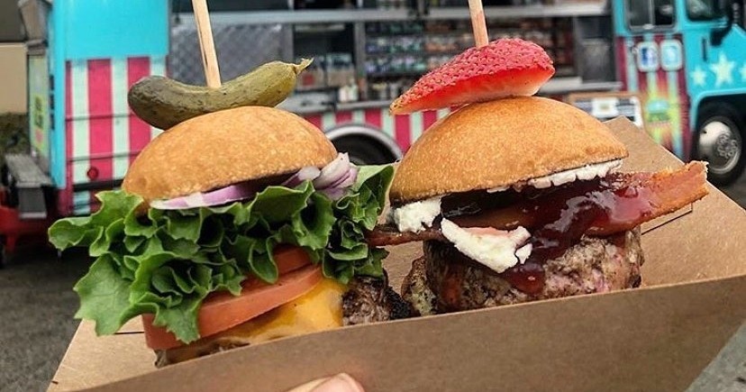 A Deep Ellum restaurant featuring 2 burgers. One burger is a traditional burger with lettuce, tomato, red onion and pickle. The other is a fig burger with goat cheese, fig jam and s strawberry for a garnish