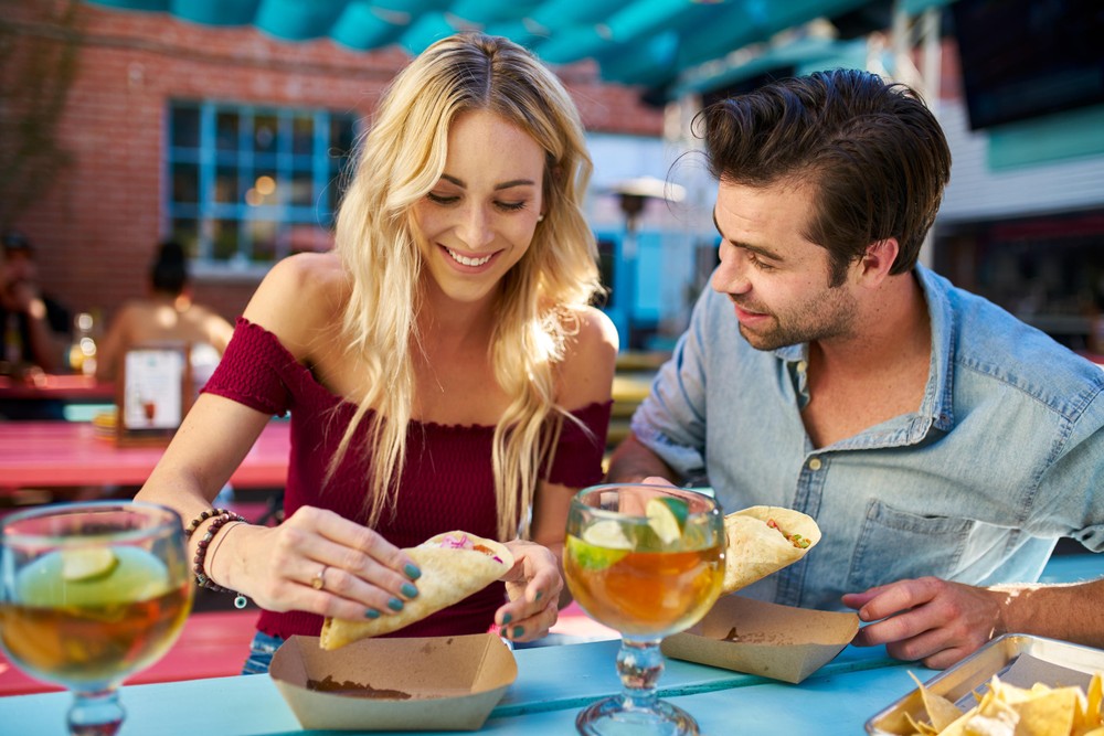 a couple eating a taco and having 2 cocktails at a restaurant in dallas during a trolley tour