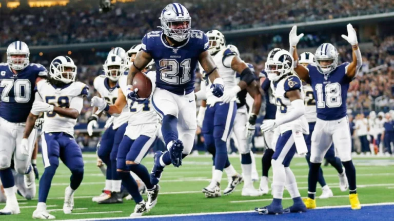 Dallas Cowboys player Ezekiel Elliott (wearing number 21) running with the football during a game against the Los Angeles Rams, with teammates and opponents around him