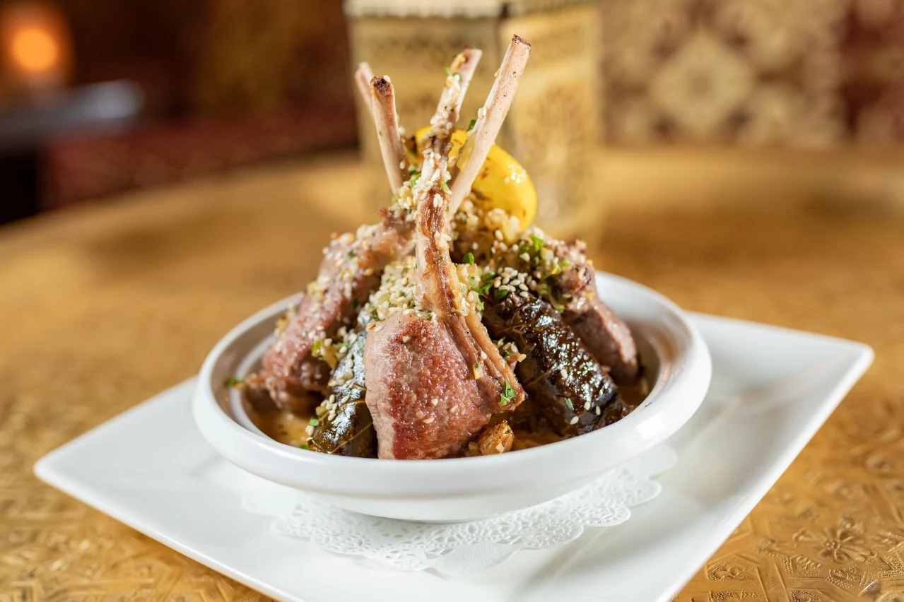 A dish of lamb chops garnished with sesame seeds and herbs, served on a white plate at Baboush restaurant in Dallas