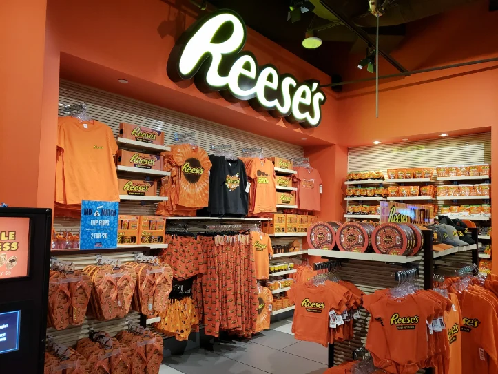 Interior of a Reese's chocolate store in Las Vegas, showcasing a variety of Reese's branded merchandise, including t-shirts, flip-flops, and candy products, all displayed under a large illuminated Reese's sign