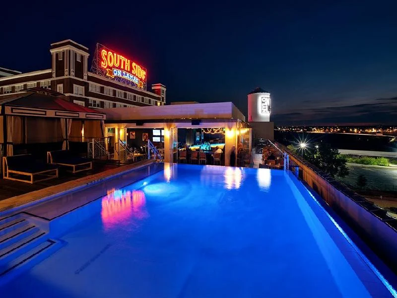 Rooftop pool area of the NYLO Dallas South Side hotel at night, featuring a lit pool, cabanas, and a neon "South Side on Lamar" sign in the background