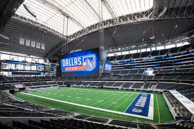 Interior view of AT&T Stadium in Dallas, showcasing the large video screen displaying "Dallas 2026" and the football field below.