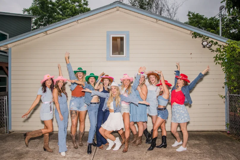 Group of women dressed in western-themed outfits celebrating a bachelorette party in Texas, posing in front of a house