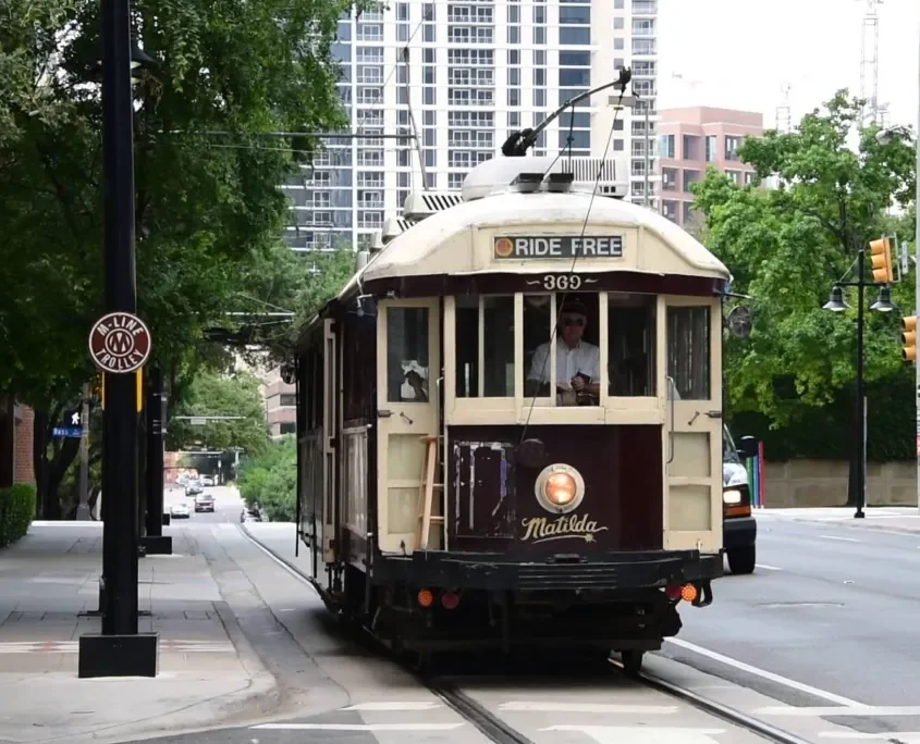 Historic trolley labeled "Matilda" in Dallas offering a free ride, moving along a tree-lined street with modern buildings in the background