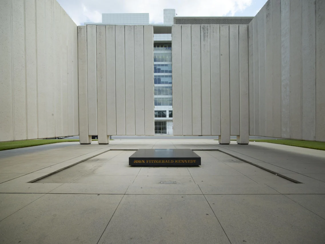 John F. Kennedy Memorial Plaza in Dallas featuring a simple, open-air, concrete structure surrounding a black marble slab engraved with John Fitzgerald Kennedy's name.