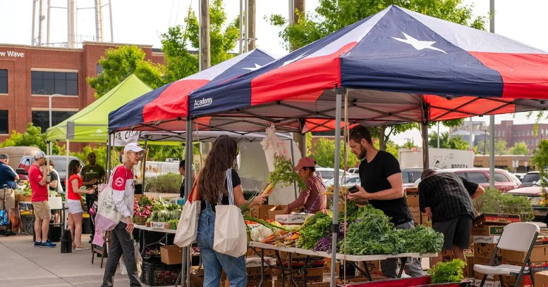 Customers shopping for fresh produce and goods under tents at a farmers market in Dallas