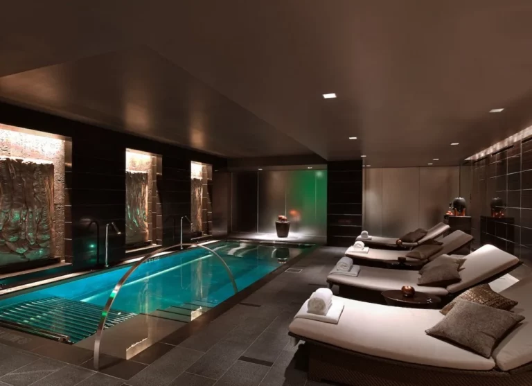 Luxurious spa in a Dallas hotel featuring an indoor pool, reclining lounge chairs with towels, and elegant wall art.