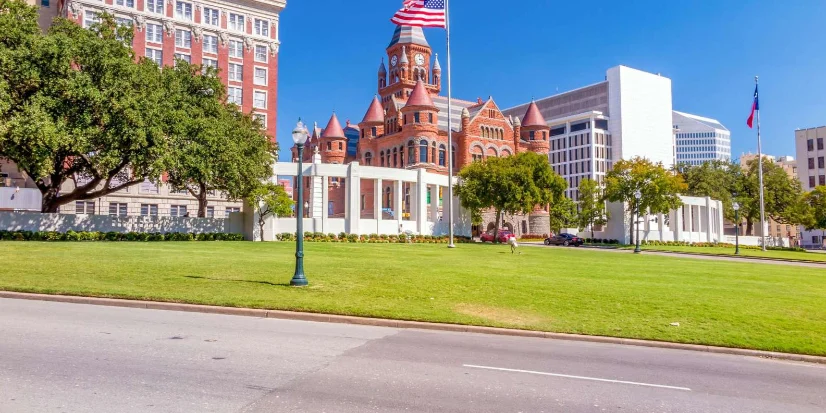 The Red Museum in Dallas with its historic architecture, lush green lawn, and American flag flying in the foreground.