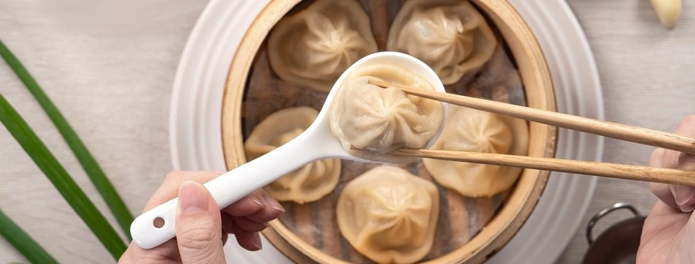 Xiao long bao (soup dumplings) being lifted with chopsticks and a spoon at a Chinatown Las Vegas restaurant